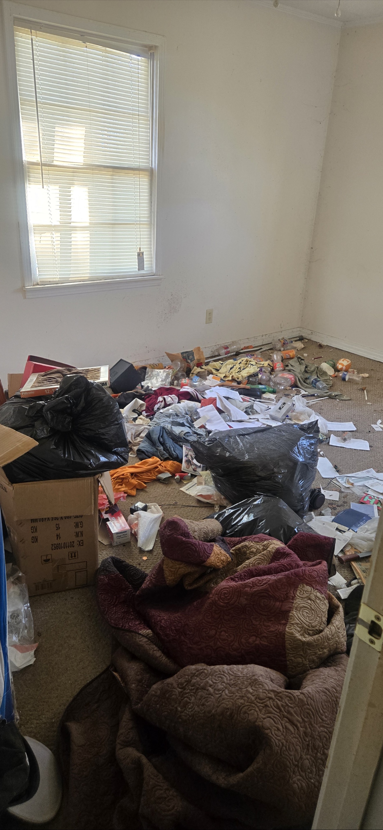 Bedroom filled with bags, clothing, boxes, and loose debris before the cleanout